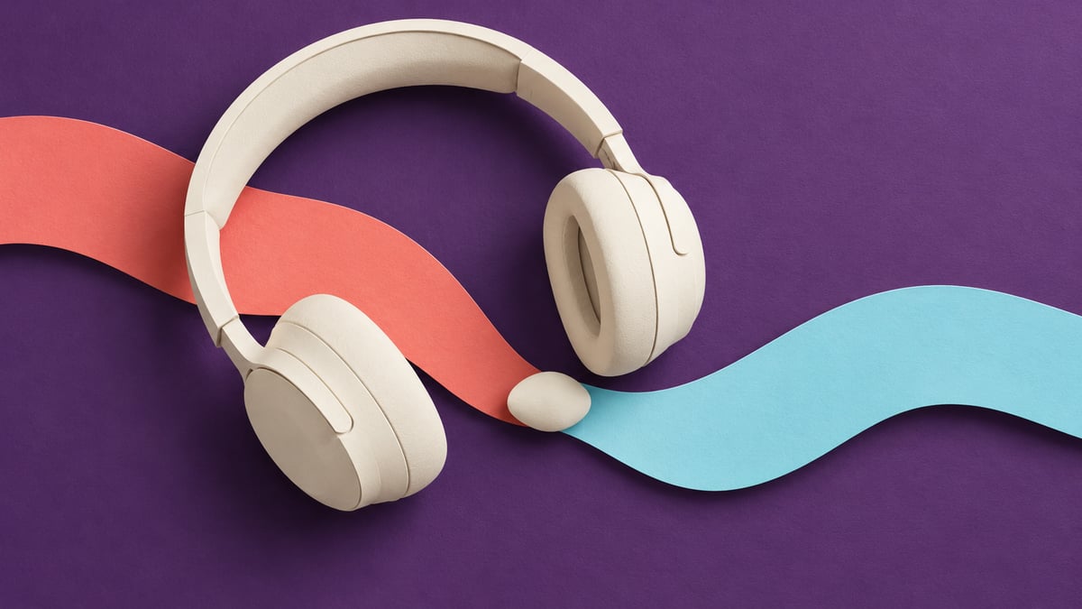Conceptual ivory headphones crossing separate coral and cyan paper ribbons on a violet background.